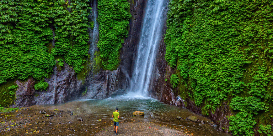 Mann står ved foten av Red Coral-fossen i Munduk, Bali