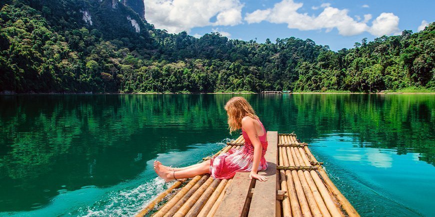 Ung jente sitter ved innsjøen i Khao Sok nasjonalpark i Thailand