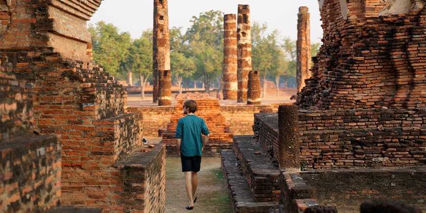 Mann vandrer ved ruinene i Sukhothai ved soloppgang